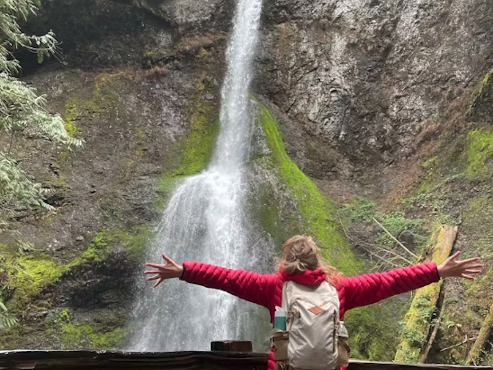 Frau breitet Arme vor Wasserfall aus