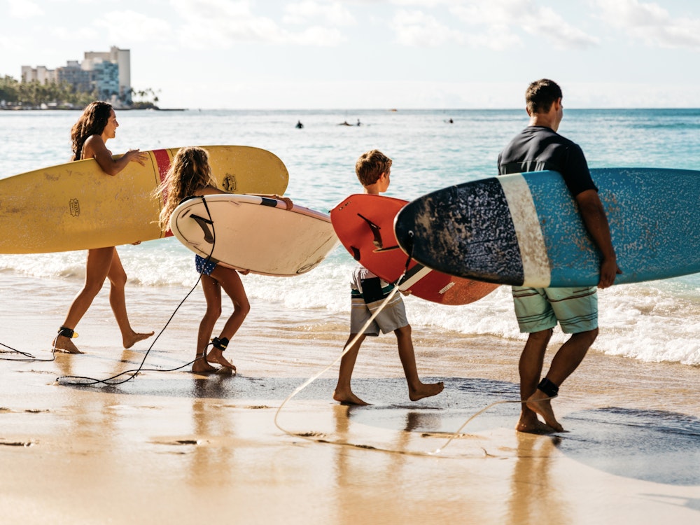 Familie loopt met surfplanken naar de zee op Hawaii