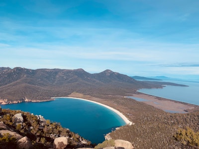 Die Wineglass Bay in Tasmanien, eine Bucht getrennt von einem Streifen Land, das Wasser und der Himmel sind blau.