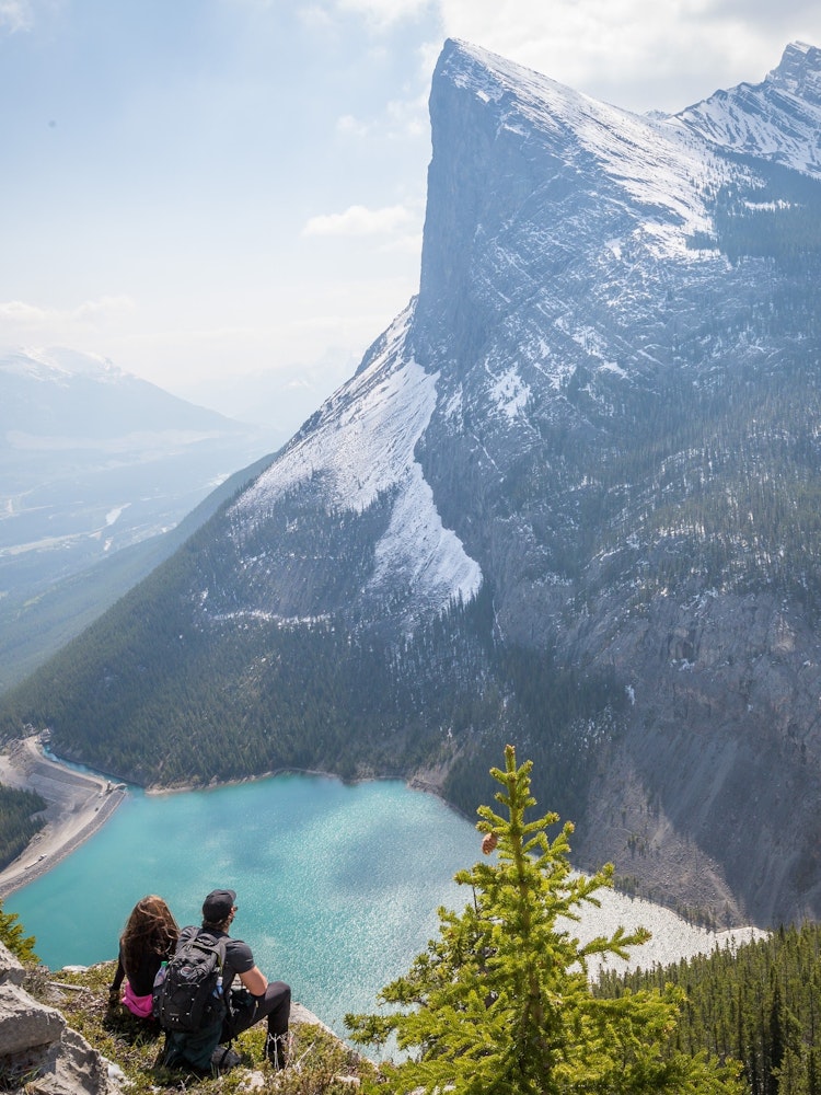 Pärchen in Kanada sitzt auf Felsvorsprung und Blickt auf Berg