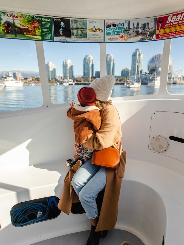 Moeder zit met haar kind op schoot op een boot, kijken naar de skyline van Vancouver