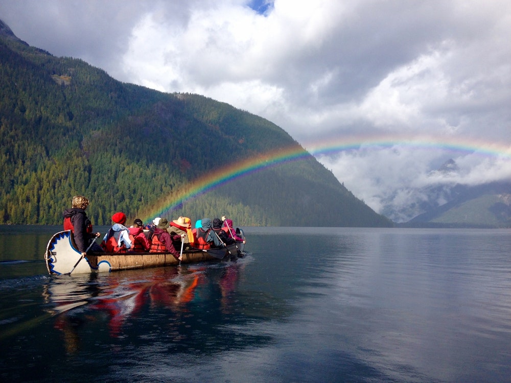 Personen fahren mit Kanu über Wasser mit Regenbogen am Horizont