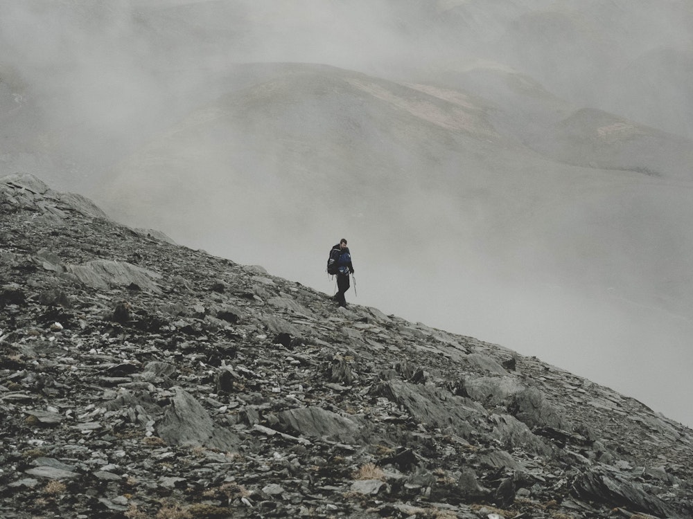 Ein einsamer Wanderer steht auf einem Geröllfeld - im Hintergrund zieht Nebel auf.