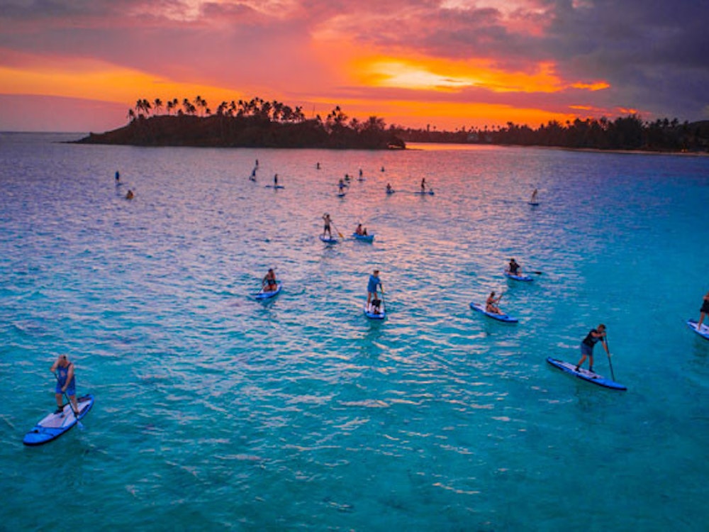 Viele Menschen machen Stand Up Paddling bei Sonnenuntergang auf den Cook islands
