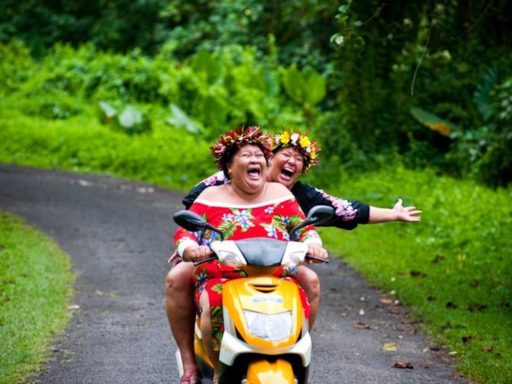 Twee vrouwen rijden op een scooter door de natuur van de Cook Eilanden