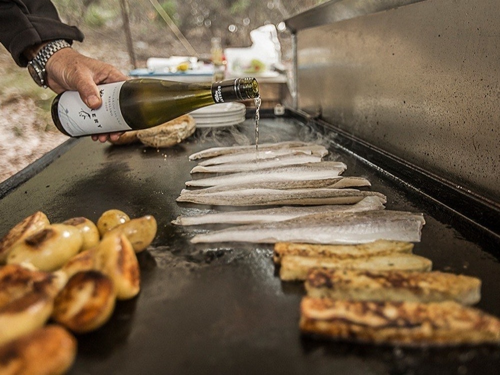 Mann übergießt Fisch auf Grill mit Wein auf Kangaroo Island
