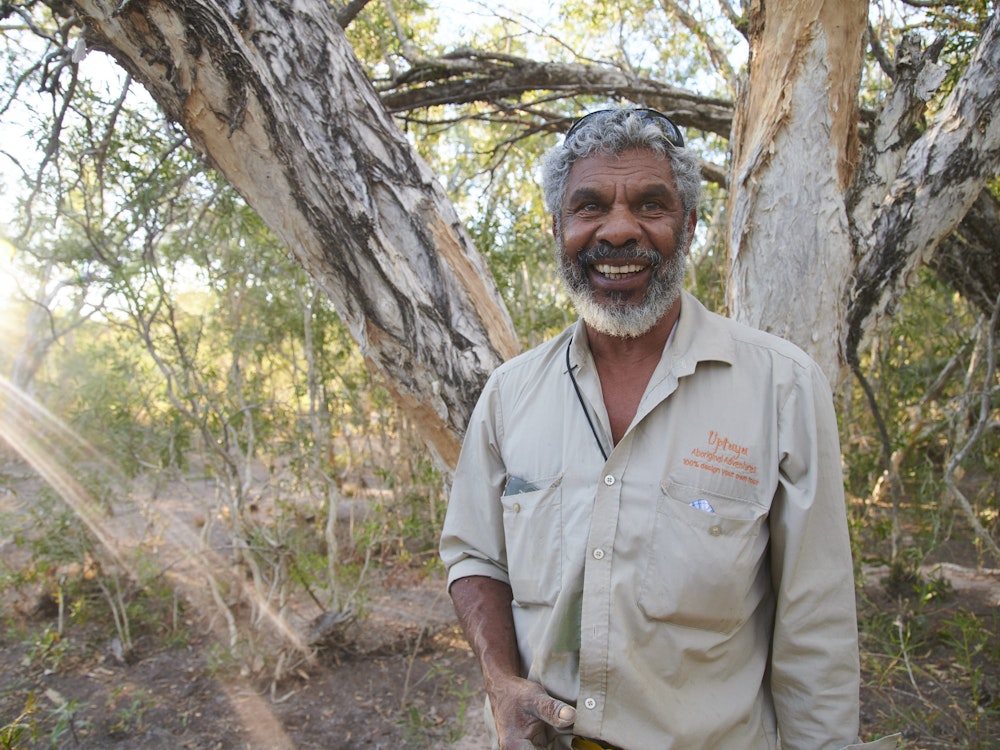 Aborigine steht in Natur und lächelt in Kamera