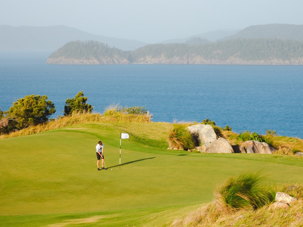 Man golft op een golfbaan met uitzicht over de kust van Hamilton Island