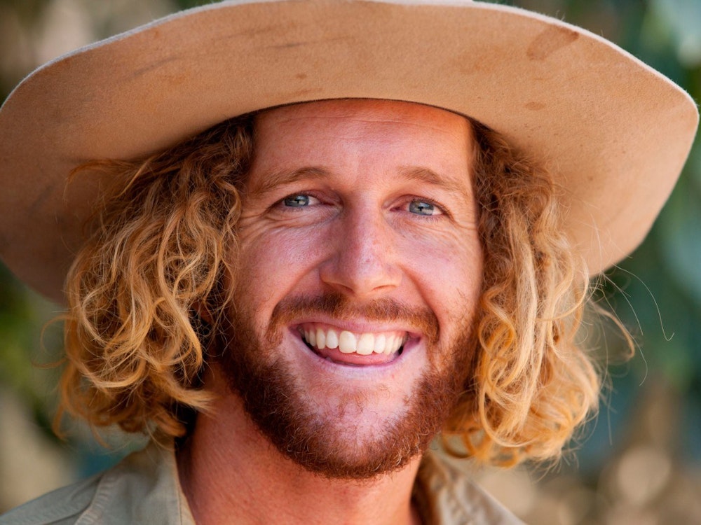 Australier mit Hut und blonden Locken lächelt in Kamera