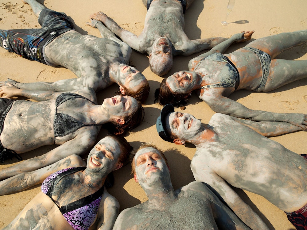 Gruppe von Personen liegt auf Sand und ist mit Schlamm eingerieben
