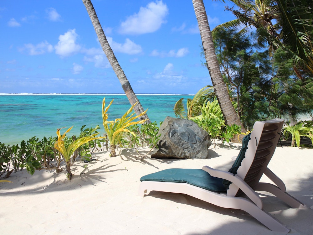 Liegestuhl am weißen Strand mit Palmen auf den Cook Islands