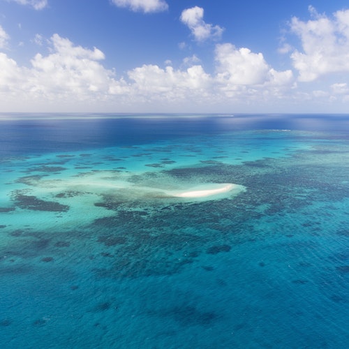 Ein türkisblau schillerndes Riff am Great Barrier Reef mit weißer Sandbank