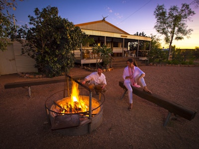 Ein Paar sitzt am Lagerfeuer vor einem Haus im Outback