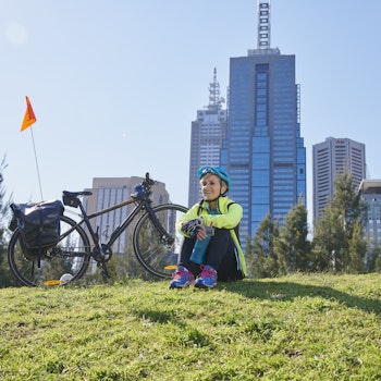 Frau sitzt auf Wiese in Melbourne mit Fahrrad im Hintergrund