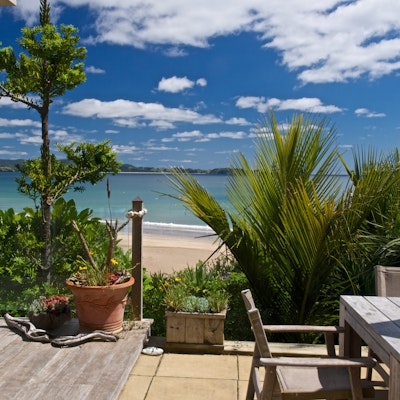 Holzterrasse mit Tisch und Stühlen mit Blick auf Strand und Bucht
