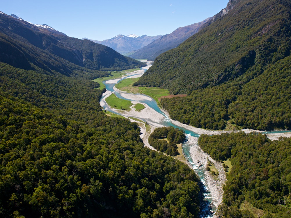 Der Makarora River schlängelt sich durch ein bewaldetes Tal im südlichen Neuseeland