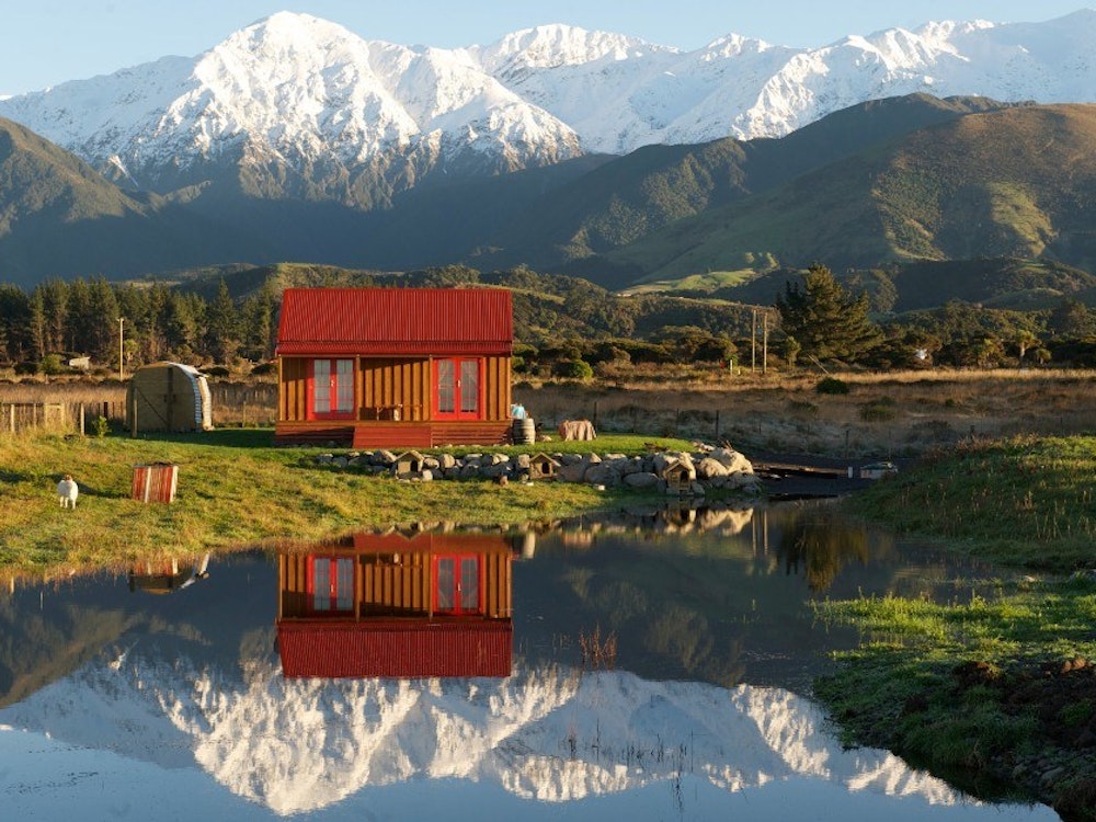 Rotes Haus vor verschneiten Berggipfeln reflektiert in stillem See