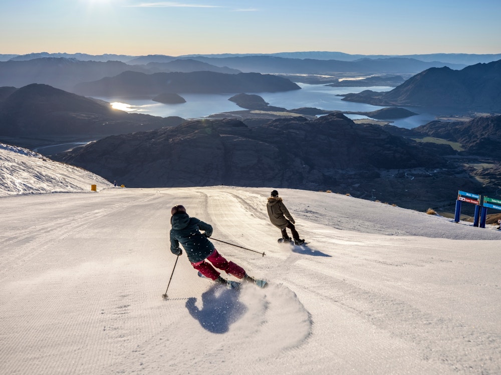 Skiër en snowboarder gaan naar beneden met op de achtergrond Lake Wanaka in Nieuw-Zeeland