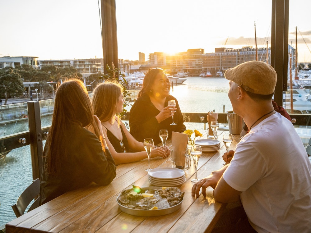 Vier mensen zitten aan een tafel met hapjes en uitzicht op de haven