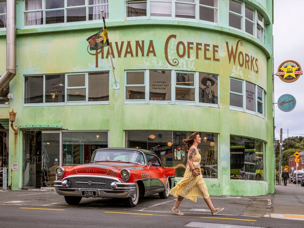 Een vrouw loopt voorbij een oldtimer voor Havana Coffee Works in Wellington