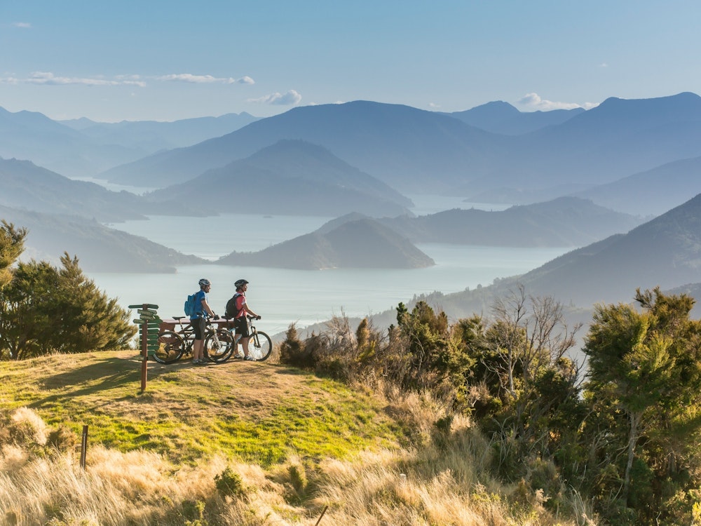 A couple on their bikes on a mountain peak overlooking the inlets of Marlborough Sounds