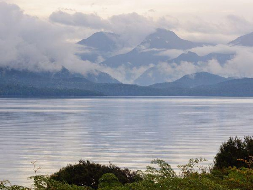 Clouds rolling over a mountain range with a lake in the foreground