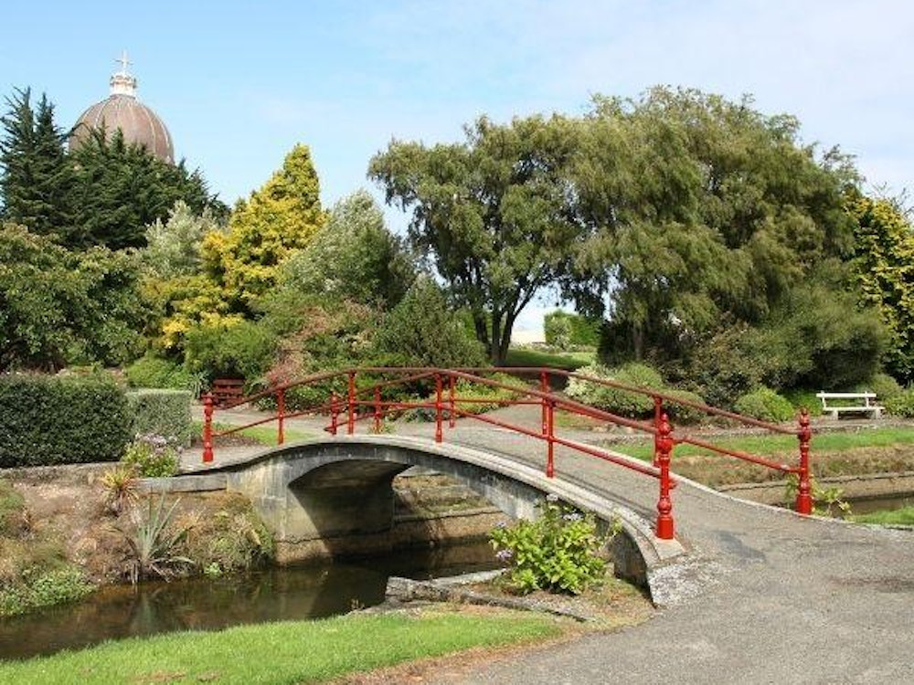 A small bridge over a stream in a park with green trees and hedges