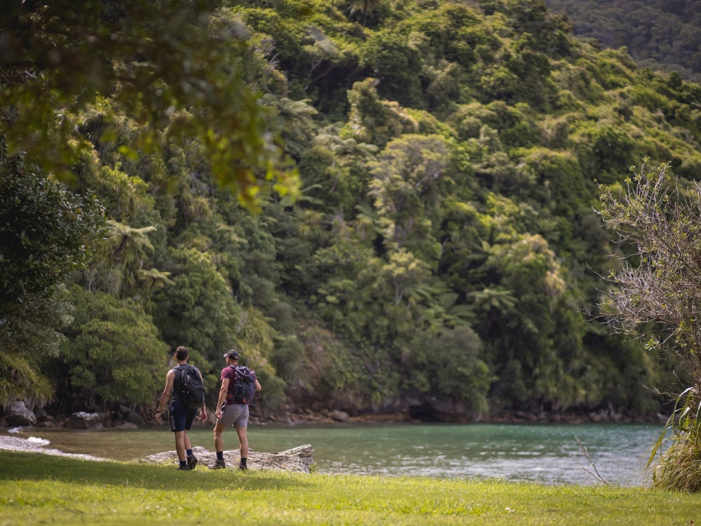 Two people walking along a green forested bay