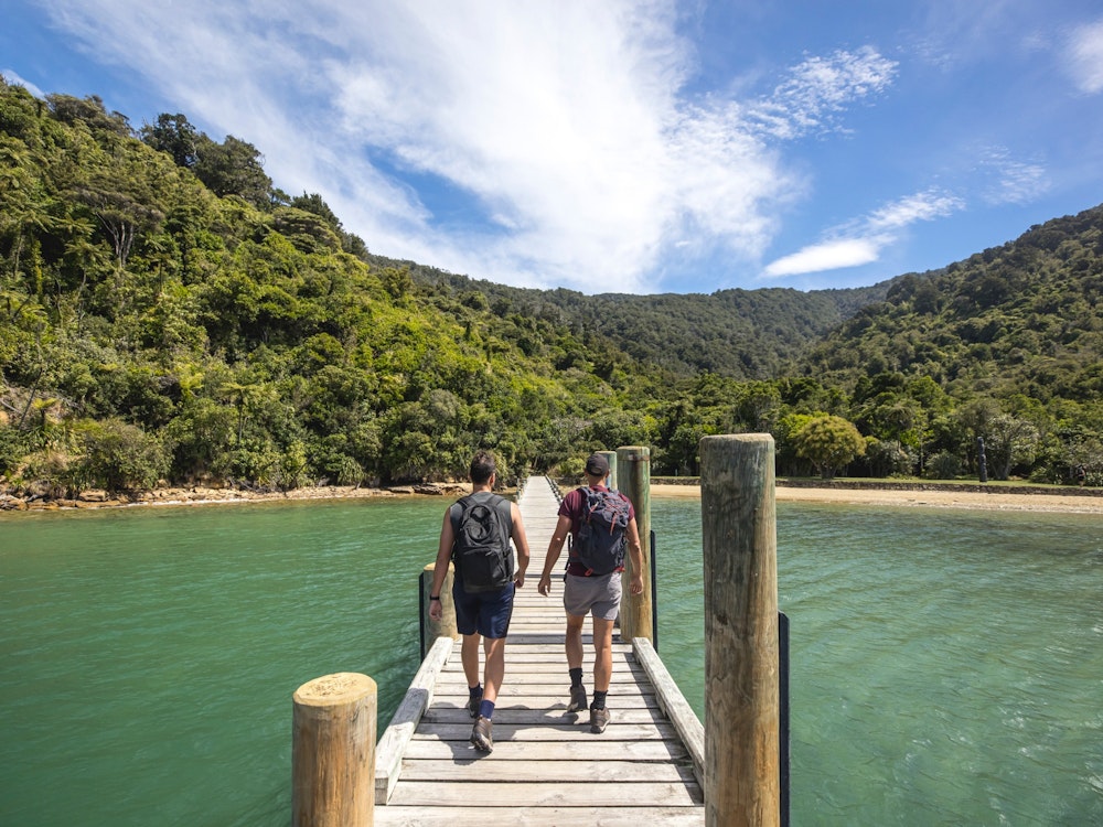 Two men with backpacks walking on a pier over the water to the shoreline