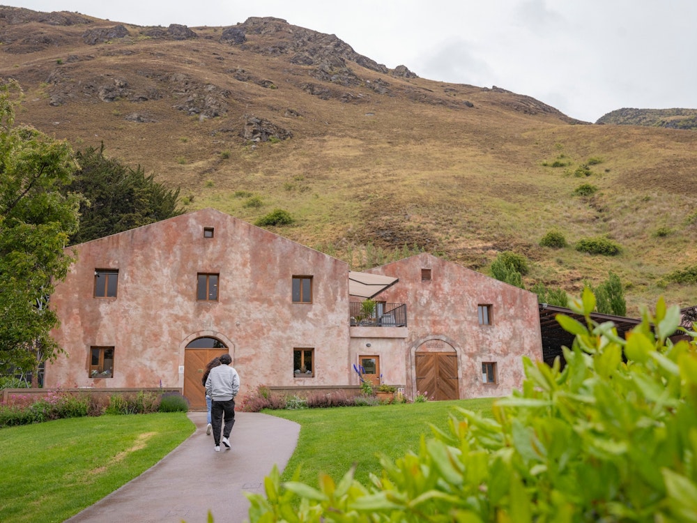 A man walking up a path to an old building with a mountain in the background