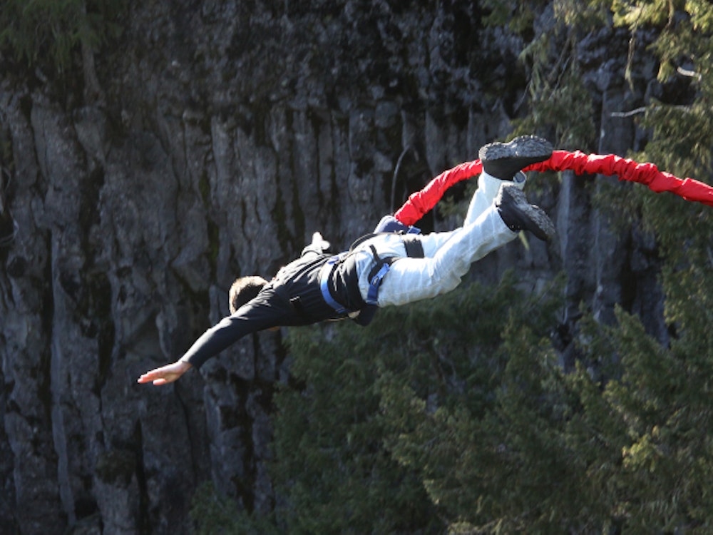 A girl with a red bungee cord strapped around her waist flying in the air