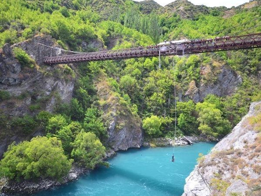 A person hanging by a rope off a bridge with a river below