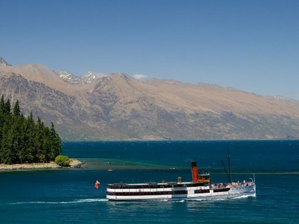 A boat cruising down a lake with mountains in the background