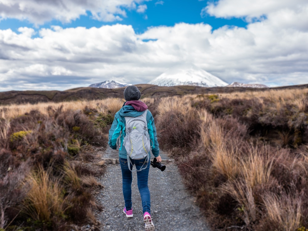 Een vrouw wandelt met camera over een pad in Tongariro National Park