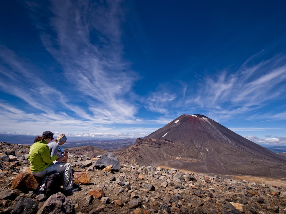 Twee vrouwen zitten op een rots met uitzicht op de vulkaan op de Tongariro Alpine Crossing