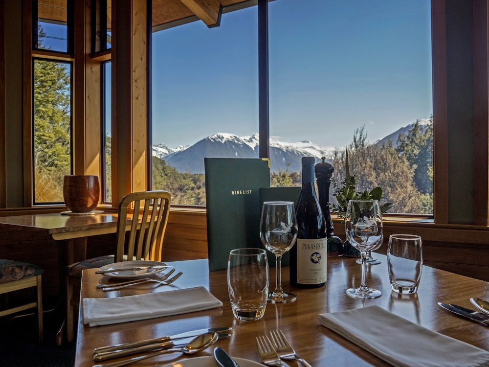 Een gedekte tafel met fles wijn en uitzicht over de met sneeuw bedekte bergen van Arthur's Pass