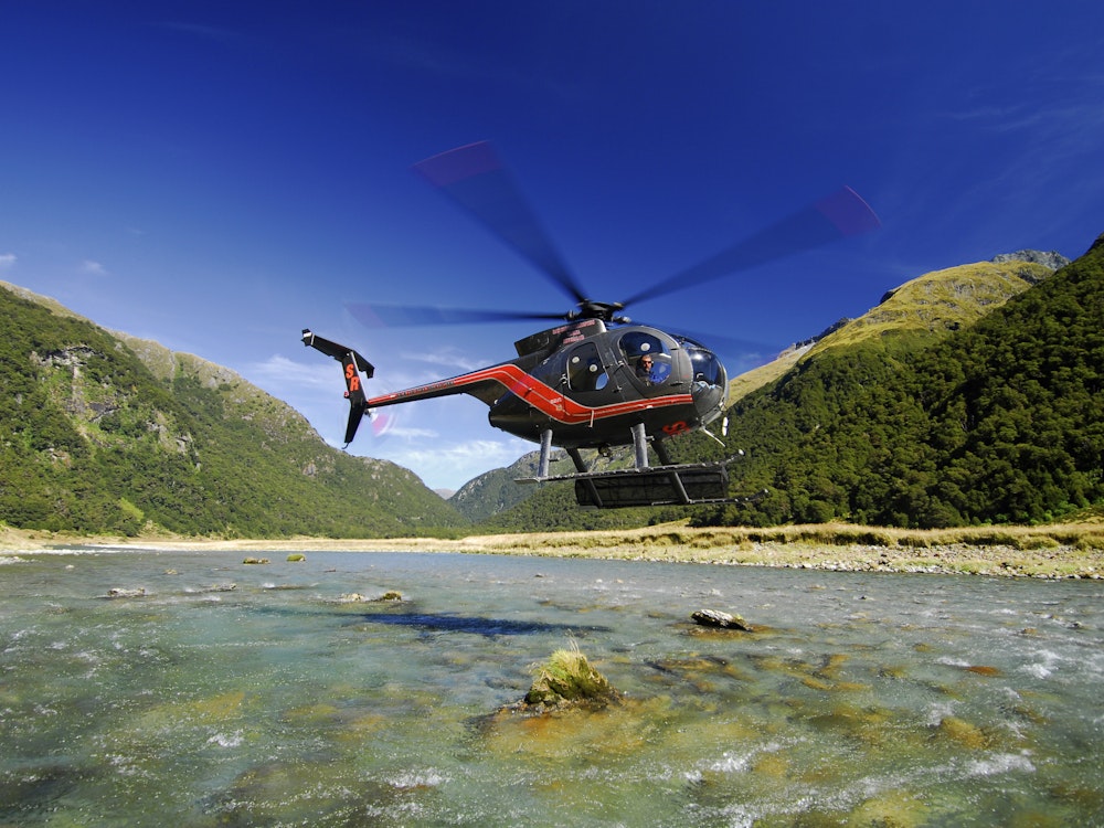 Een helikopter dat gaat landen in een natuurlijk gebied met bergen op de achtergrond in Nieuw-Zeeland