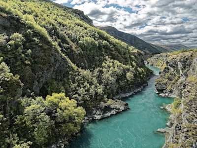 Uitzicht over een vallei in Nieuw-Zeeland met groene bergen en helderblauw water