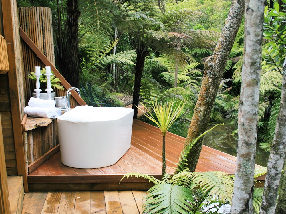 Een luxe badkamer met bad in de buitenlucht, uitkijkend op het regenwoud nabij Auckland, Nieuw-Zeeland