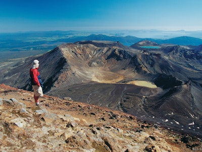 Een man wandelt over de Tongariro Alpine Crossing en bekijkt het weidse uitzicht