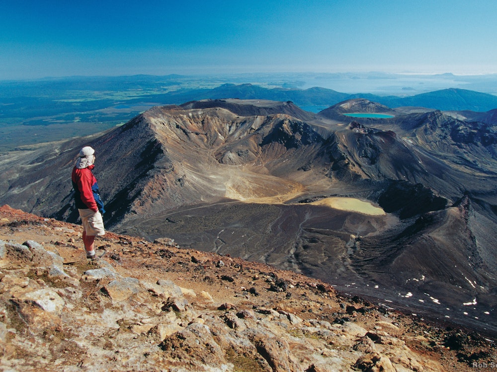 Een man wandelt over de Tongariro Alpine Crossing en bekijkt het weidse uitzicht