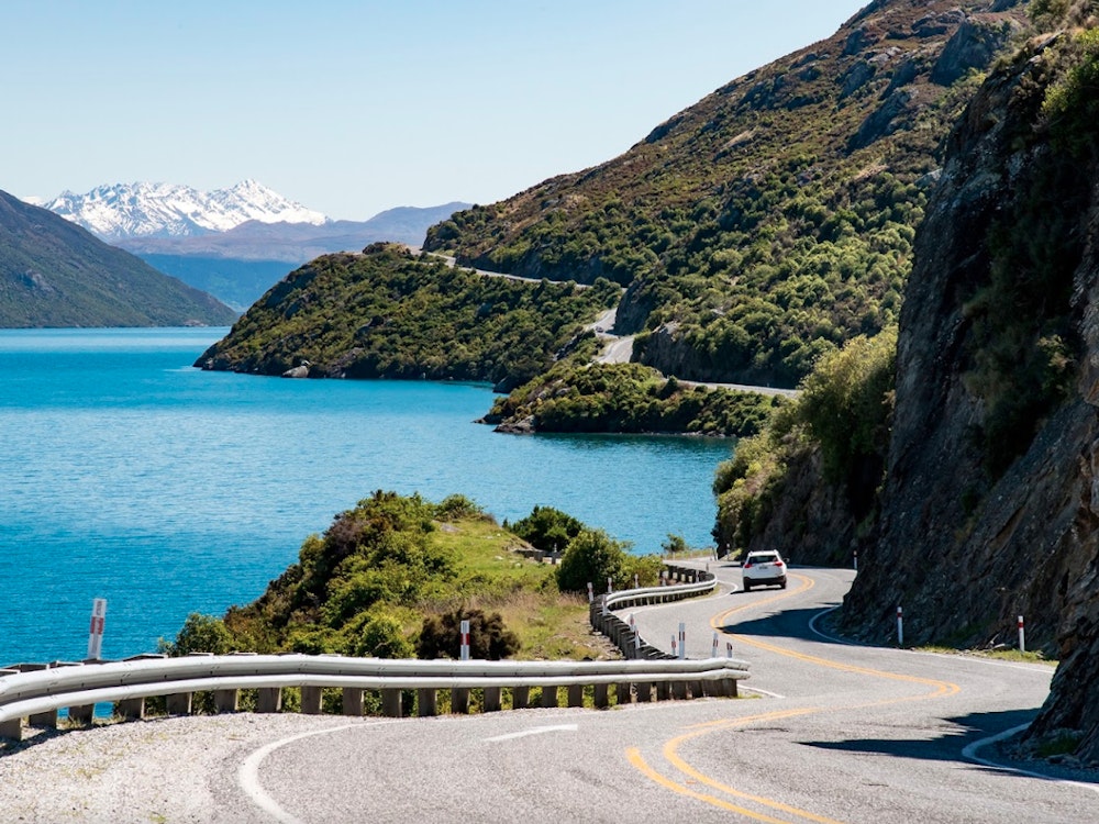 Een auto rijdt op een slingerende weg langs een meer en de bergen in Nieuw-Zeeland