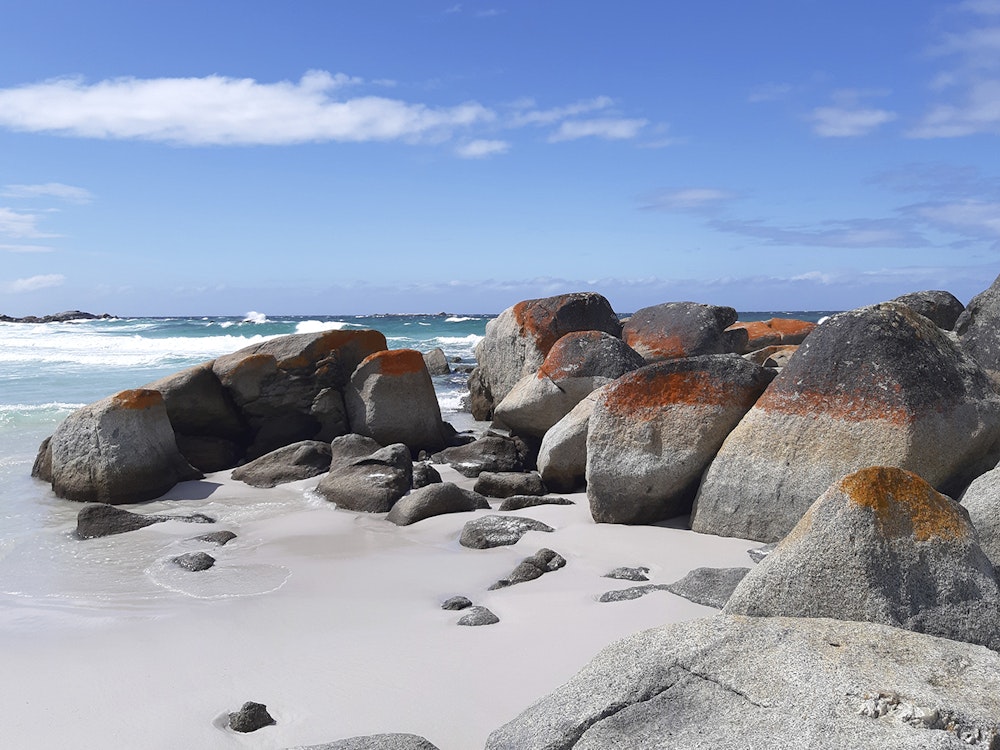 Wit strand met blauwe zee en een blauwe lucht en rotsen met oranje.