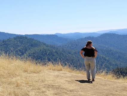 Eine Frau steht auf einer Wiese, Ausblick auf eine kleine Bergkette