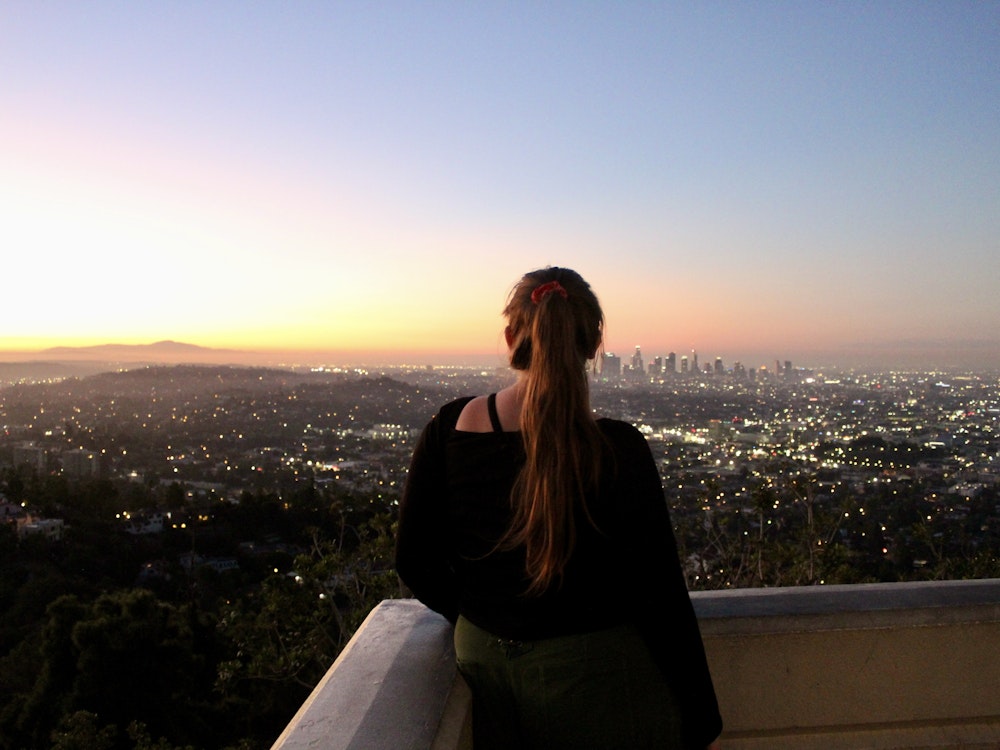 Eine Frau schaut von oben über Los Angeles, die Sonne geht langsam auf.