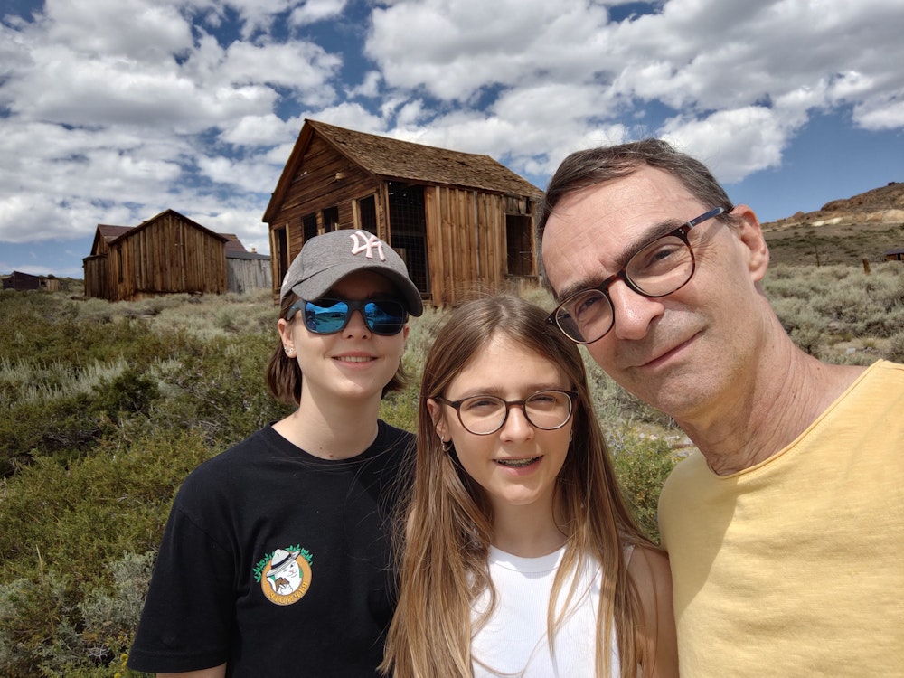 Eine Familie aus einem Vater und zwei Töchtern vor Hütten in einer wüstenähnlichen Gegend